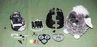 Furbík rozebraný na prvočinitele. Zleva: vnitřnosti, tužkové baterie, tvrdý skelet, svlečka. V popředí: mechanismus uší a obličejové partie